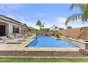 Backyard featuring a sparkling blue swimming pool with travertine tile, surrounded by lush landscaping and lounge chairs at 23097 N 95Th Dr, Peoria, AZ 85383