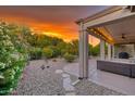Spacious backyard featuring desert landscaping, a covered patio, and colorful sunset sky at 15928 W Zinnia Ct, Surprise, AZ 85374