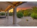 Covered patio with outdoor seating amidst lush desert landscaping and a gorgeous sunset backdrop at 15928 W Zinnia Ct, Surprise, AZ 85374