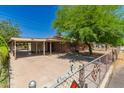 A single-story brick house with a carport and spacious driveway, surrounded by lush trees and a chain-link fence at 6100 N 36Th Ave, Phoenix, AZ 85019