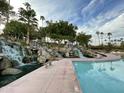 Scenic water feature with multiple waterfalls, a pool, and lush landscaping with palm trees in a community at 2301 E Beachcomber Dr, Gilbert, AZ 85234