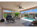 Relaxing outdoor patio with a ceiling fan, seating, a grill, and a beautiful pool with a waterfall feature at 4239 E Azalea Dr, Gilbert, AZ 85298