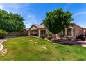 A spacious backyard with mature landscaping, including trees, shrubs, and a covered patio at 7231 W Lone Cactus Dr, Glendale, AZ 85308