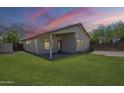 Spacious backyard featuring a lush green lawn, covered patio, and desert landscaping at dusk at 9330 E Plana Ave, Mesa, AZ 85212