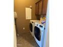 The laundry room features a washer, dryer, overhead cabinet, and a mop in a room with brown walls at 29935 W Roosevelt St, Buckeye, AZ 85396