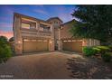 Home exterior featuring a three-car garage, balconies, desert landscaping, and a brick driveway at 23081 S 223Rd Way, Queen Creek, AZ 85142