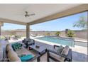 Relaxing outdoor living space with a covered patio, comfortable seating, and a sparkling pool with waterfall feature at 18000 W Thistle Landing Dr, Goodyear, AZ 85338
