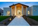 A grand entrance with an arched doorway framed by pillars and a lighted walkway leads to a modern, stucco home at 9820 N 87Th Pl, Scottsdale, AZ 85258