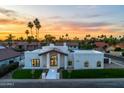 The home has a bright exterior with a grand entrance and manicured lawn, complemented by palm trees and a colorful sunset backdrop at 9820 N 87Th Pl, Scottsdale, AZ 85258