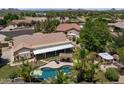 Stunning aerial view of a backyard featuring a pool, tiki hut, covered patio, and lush landscaping at 7315 W Monte Lindo Ln, Glendale, AZ 85310