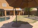 Backyard featuring a pool, green space, and a patio with an umbrella for shade at 35743 W Cartegna Ln, Maricopa, AZ 85138