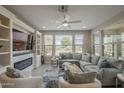 Inviting living room with a cozy fireplace, built-in shelves, ceiling fan, and large windows for natural light at 36042 N Desert Tea Dr, Queen Creek, AZ 85140