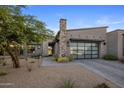 Contemporary home showcases desert landscaping, a stone chimney, and a sleek glass garage door at 12311 E Black Rock Rd, Scottsdale, AZ 85255