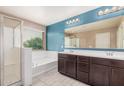 Bathroom featuring a large soaking tub, glass-enclosed shower, dual sinks with dark cabinets, and tile flooring at 15551 W Poinsettia Dr, Surprise, AZ 85379