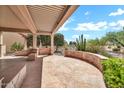 Covered patio with stone flooring and decorative knee wall overlooks native desert landscaping at 15534 W Big Sky Dr, Surprise, AZ 85374