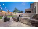 Stylish outdoor area featuring a built-in barbecue and stone fireplace under the ambient glow of string lights at 22259 N 102Nd Ln, Peoria, AZ 85383