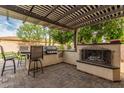 Outdoor kitchen boasts a built-in grill, bar seating, and a cozy fireplace under a pergola at 27007 N 20Th Ln, Phoenix, AZ 85085
