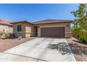 A cozy tan home featuring a brown garage door, desert landscaping, and a spacious driveway at 17296 W Molly Ln, Surprise, AZ 85387