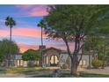 Charming home with desert landscaping and palm trees, a stone chimney, and an arched entry under a colorful sunset at 5402 E Cortez Dr, Scottsdale, AZ 85254