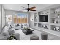 Bright living room features large windows, comfortable seating, ceiling fan, and built-in shelving around the television at 25974 W Horsham Dr, Buckeye, AZ 85396