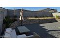 Entertaining backyard featuring a rock wall, decorative gravel, seating area with outdoor furniture and decorative umbrella at 18230 W Poston Dr, Surprise, AZ 85387