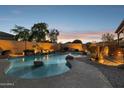 An outdoor pool with rock features, lighting, and mature trees offers a relaxing backyard space at 18121 E San Luis Dr, Gold Canyon, AZ 85118