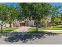 Inviting two-story home with a paved driveway leading to a garage, lush green lawn, and mature trees, showcasing its serene setting at 20409 W Thayer St, Buckeye, AZ 85396