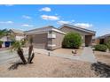 Single-story home with desert landscaping featuring mature plantings and an attached two-car garage in a quiet neighborhood at 12410 W Flores Dr, El Mirage, AZ 85335