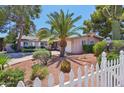Well maintained front yard featuring mature palm and shade trees and desert landscaping behind a white picket fence at 8637 E Solano Dr, Scottsdale, AZ 85250