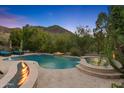 Resort-style backyard featuring a pool, spa, tanning ledge, fire features, lush landscaping, and mountain views at 26036 N 85Th Dr, Peoria, AZ 85383