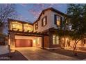 Two-story home with stone accents and a balcony above the garage, beautifully illuminated at twilight at 20689 W Valley View Dr, Buckeye, AZ 85396