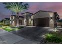 Twilight shot of an estate featuring a large brick driveway and desert landscaping with a palm tree at 30404 N 131St Dr, Peoria, AZ 85383