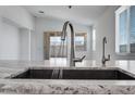 Close-up of kitchen sink featuring a modern faucet, granite countertops and an open, bright living space at 18153 W Hiddenview Dr, Goodyear, AZ 85338