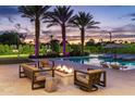 Inviting backyard at dusk featuring a pool, a cozy fire pit lounge, and palm trees with vibrant uplighting at 9148 N 66Th Pl, Paradise Valley, AZ 85253