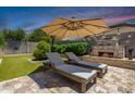 Relaxing backyard featuring an outdoor fireplace, travertine patio, and two lounge chairs under a large umbrella at 21275 E Russet Rd, Queen Creek, AZ 85142