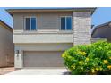 Two-car garage of a two-story home with stone and textured facade details and green shrub at 2067 N Marketside Ave, Buckeye, AZ 85396
