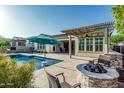 Well-appointed backyard featuring a pool, patio cover, fire pit and lush landscaping at 20595 W Pasadena Ave, Buckeye, AZ 85396