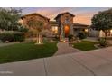 Charming home with lush green lawn, stone accents, and a paver walkway leading to a well-lit entrance under a colorful sunset at 3907 E Carob Dr, Gilbert, AZ 85298