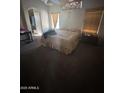 A dim bedroom featuring light colored carpet, a ceiling fan, a tan bedspread, a window, and decor at 16696 W Culver St, Goodyear, AZ 85338