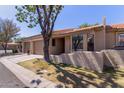 Exterior view of a single-story home showcasing a low stucco wall, desert landscaping and large shade tree at 1021 S Greenfield Rd # 1211, Mesa, AZ 85206