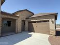 View of the home's stone-accented facade, three car garage, and covered entry at 17308 W Royal Palm Rd, Waddell, AZ 85355