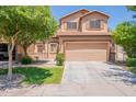 Two-story tan home showcasing a two-car garage, complimented by a lush lawn and mature trees at 931 S Racine Ln, Gilbert, AZ 85296