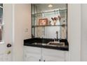 This wet bar features a black countertop, mirror backsplash, glass shelving, and white cabinets at 4015 N 78Th St # 135, Scottsdale, AZ 85251