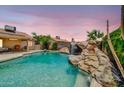 Backyard pool area featuring a rock waterfall, lush landscaping, and a cozy seating area at 10943 W Alice Ave, Peoria, AZ 85345