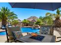 Backyard pool with a fire pit table and lounge chairs under a shaded umbrella for relaxation and entertainment at 1078 W Desert Aster Rd, San Tan Valley, AZ 85143