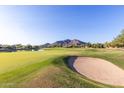 Picturesque golf course view featuring vibrant green grass, a sand trap, pond, and mountain backdrop at 7152 E Night Glow Cir, Scottsdale, AZ 85266