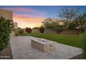 Beautiful backyard featuring a stone fire pit, putting green, manicured lawn, mature trees, and vibrant bougainvillea at 11717 W Red Hawk Dr, Peoria, AZ 85383