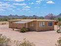 A charming tan single-story house with a metal roof sits on a vast desert landscape at 270 S Ralston Rd, Maricopa, AZ 85139