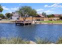 Scenic view of a community pond featuring a wooden dock, gazebo, lush greenery, and surrounding residential homes at 36956 W Santa Maria St, Maricopa, AZ 85138