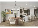 Open-concept dining area with stylish chandelier, flowing into a modern kitchen with an island and stainless hood at 19028 W Rose Ln, Waddell, AZ 85355